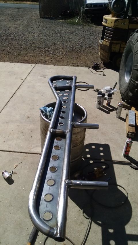 1985 Jeep CJ7 - A custom-fabricated steel bumper or roll cage component is shown lying on a concrete surface, supported by a metal barrel. Several cans of…