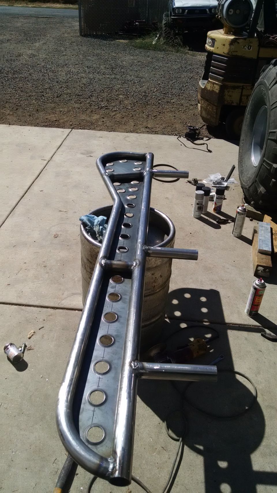Custom steel bumper/roll cage part with circular cutouts, resting on a barrel.