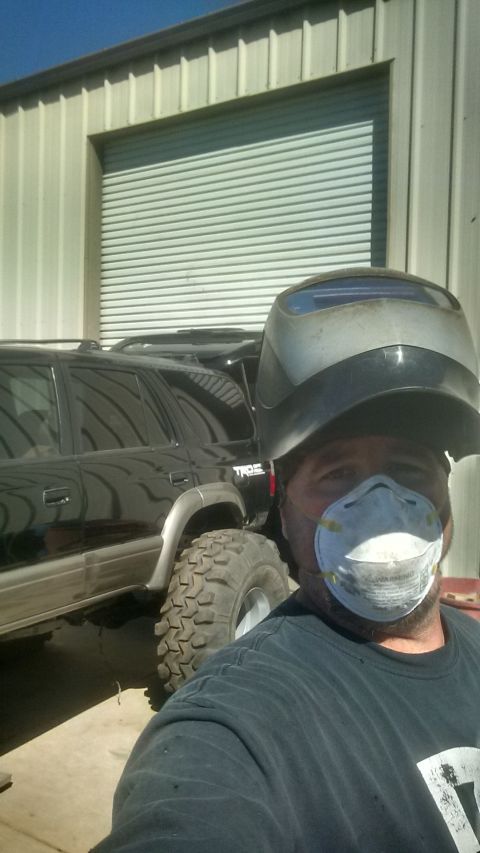 1985 Jeep CJ7 - A person wearing a welding mask and respirator takes a selfie in front of a black SUV with large off-road tires. The vehicle is parked in f…
