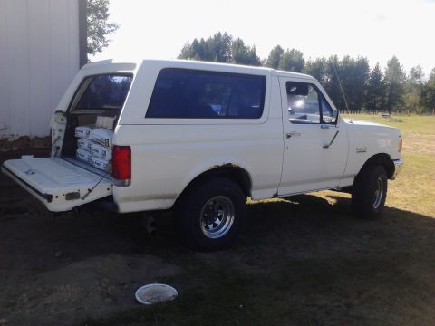 1990 Ford Bronco - A white Ford Bronco with its tailgate down is loaded with several bags of what appears to be cement mix. The vehicle is parked on a grassy…