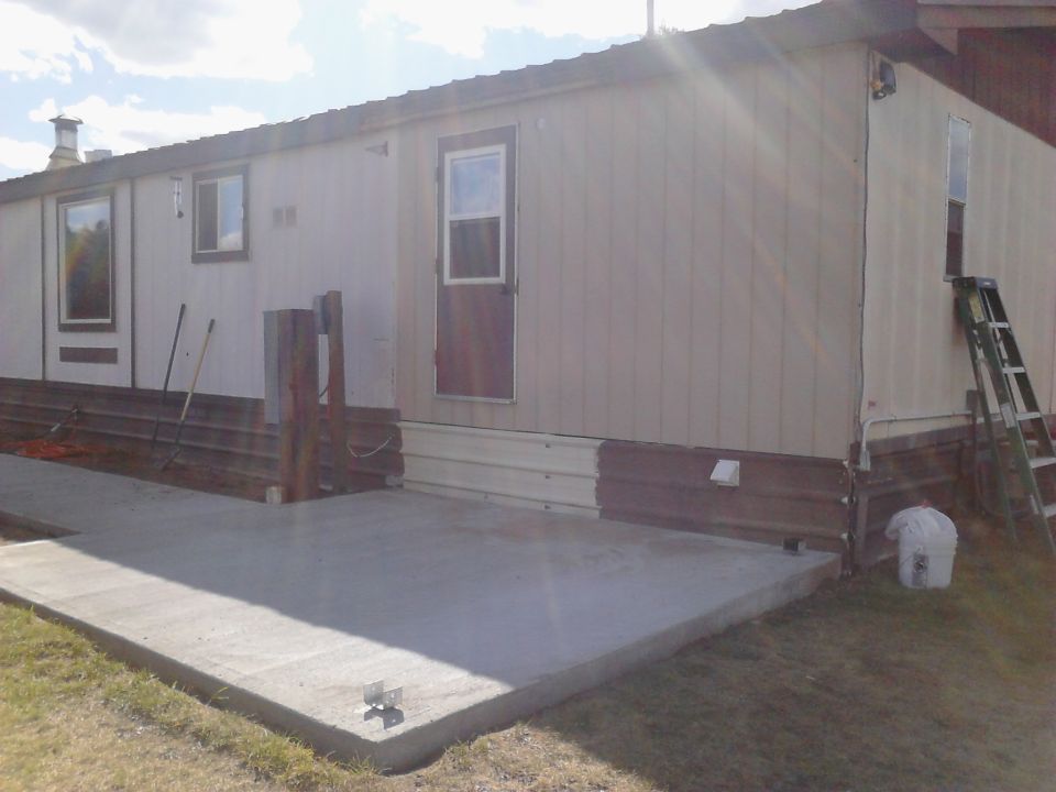 Side view of a mobile home with a concrete patio and a ladder.
