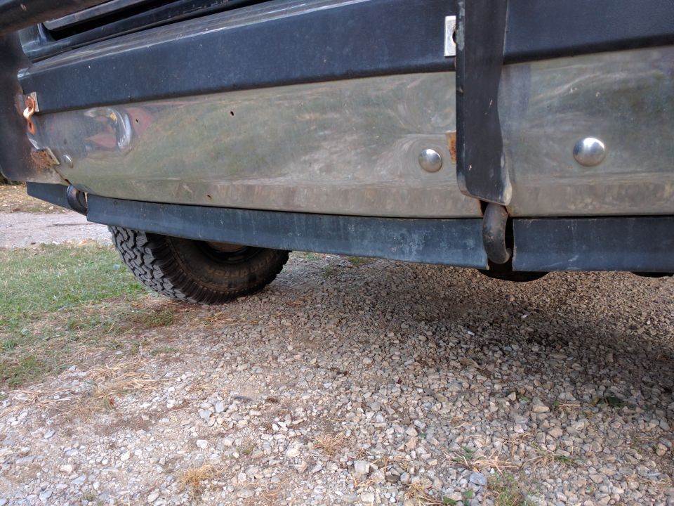 Rear bumper and tire of a dark SUV on a gravel surface.
