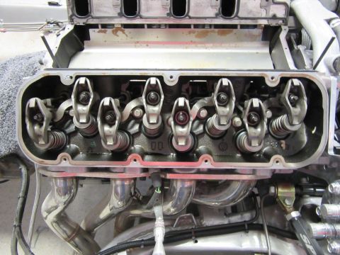 Internal view of a V8 engine cylinder head with rocker arms and exhaust headers.