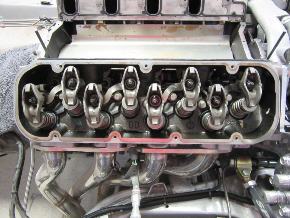 Internal view of a V8 engine cylinder head with rocker arms and exhaust headers.