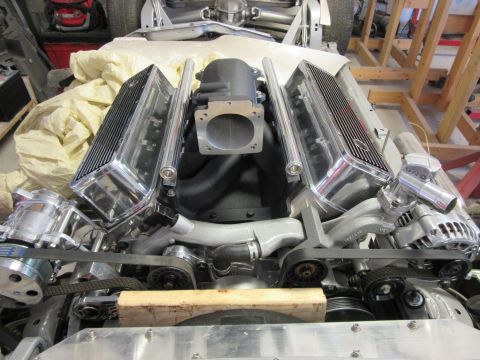 Polished V8 engine with chrome valve covers and intake manifold in a workshop.