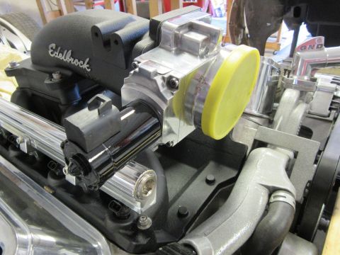 Close-up of engine parts: Edelbrock intake, throttle body with yellow cap, chrome fuel rails.