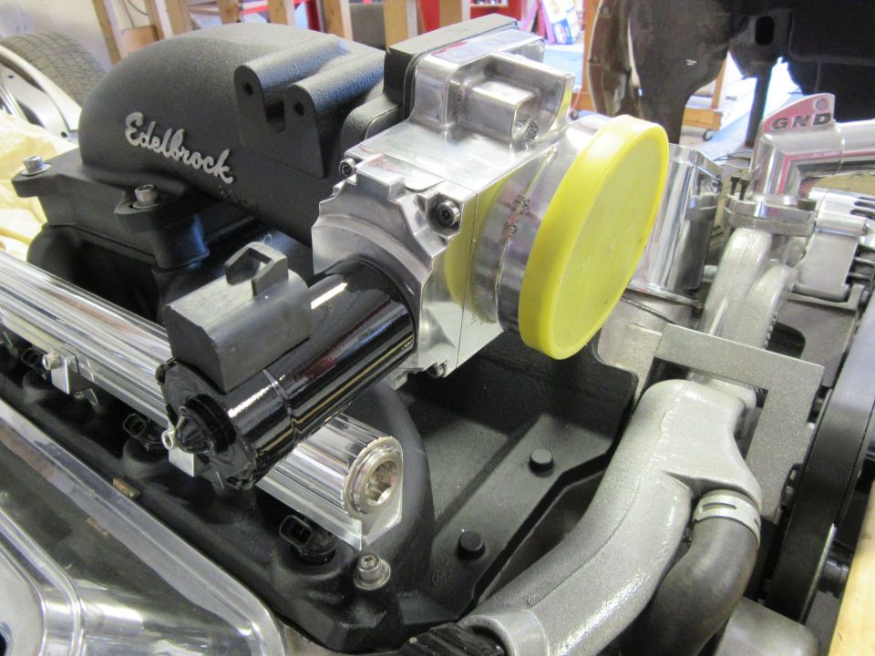 Close-up of engine parts: Edelbrock intake, throttle body with yellow cap, chrome fuel rails.