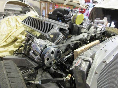Polished V8 engine with Edelbrock intake and Champion radiator cap in vehicle chassis.