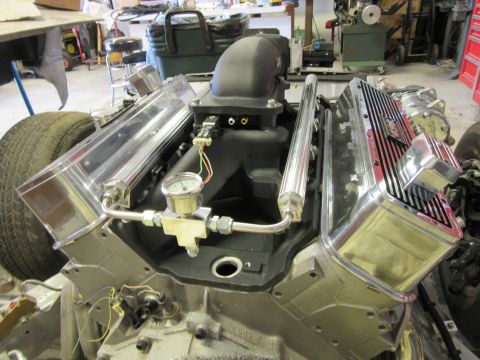 Close-up of a V8 engine with polished valve covers and intake manifold, showing a fuel pressure gauge.