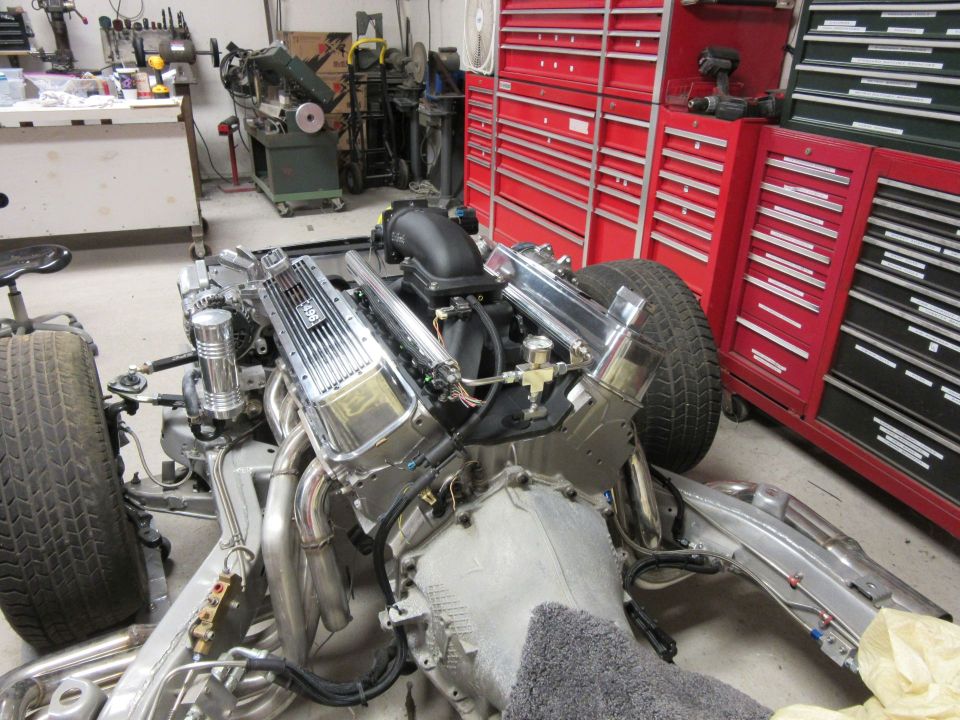 Engine and chassis in a workshop, chrome valve covers visible.