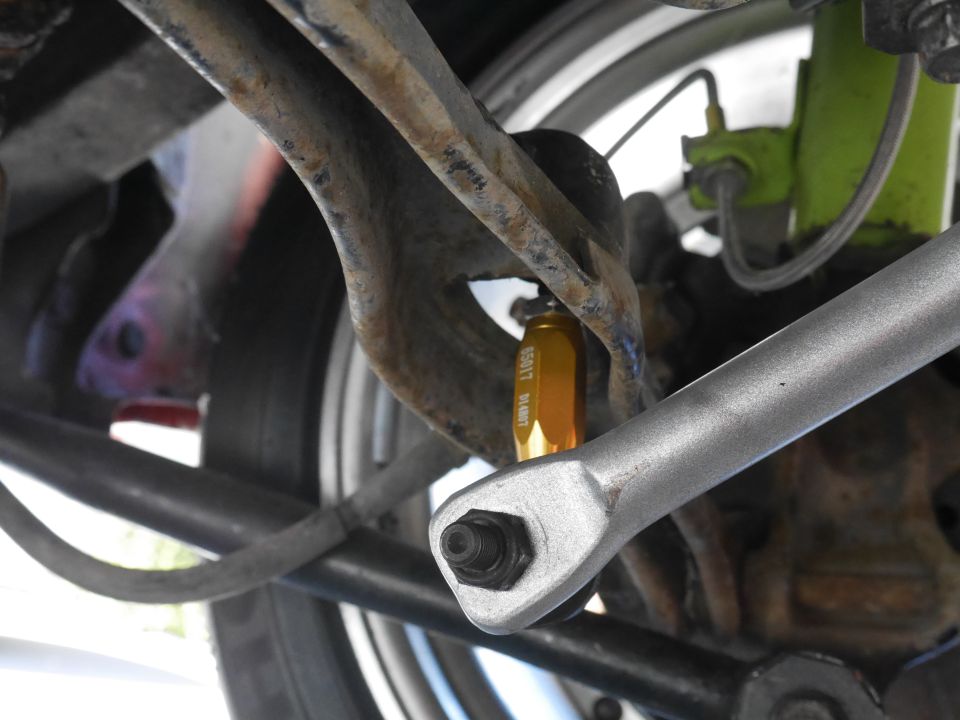 Underside of vehicle suspension with silver sway bar end link and gold adjustable component.