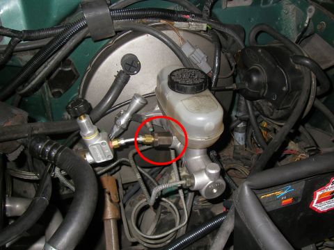 1990 Ford Bronco - A close-up view of the brake master cylinder and brake booster assembly in a vehicle engine bay. A red circle highlights a brass fitting co…