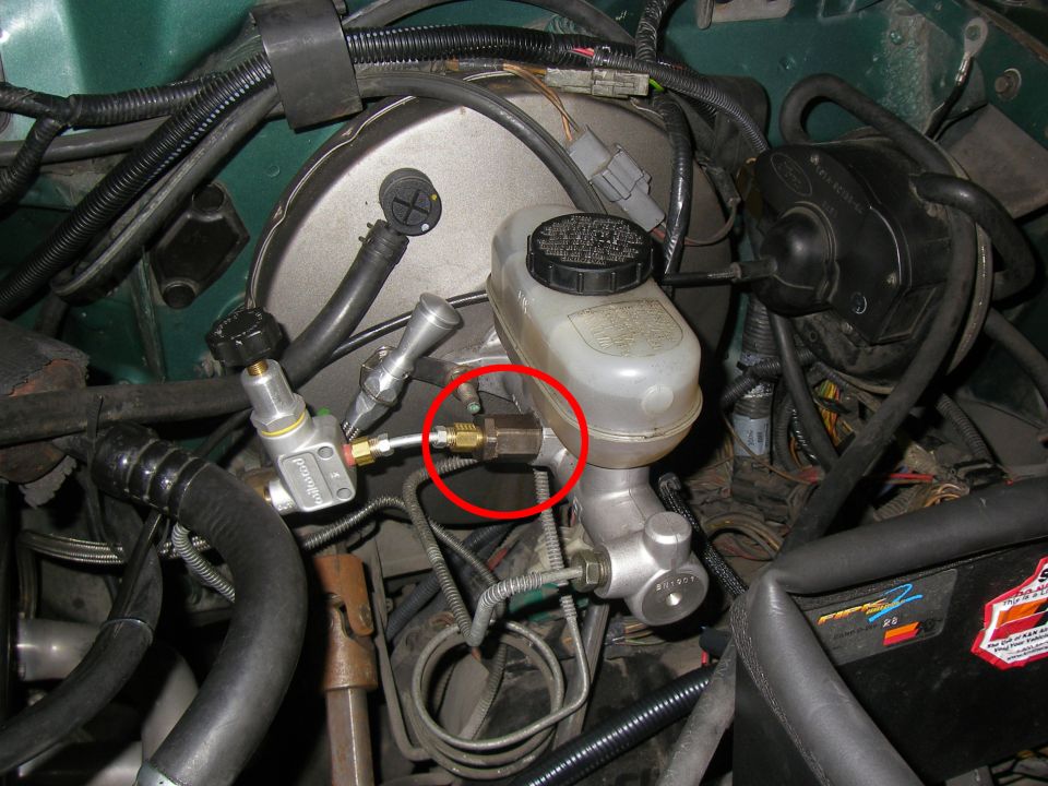 Close-up of brake master cylinder and booster assembly, with a brass fitting circled.