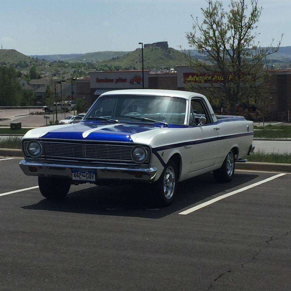 White and blue 1966 Ford Ranchero parked in a lot, hills in background.