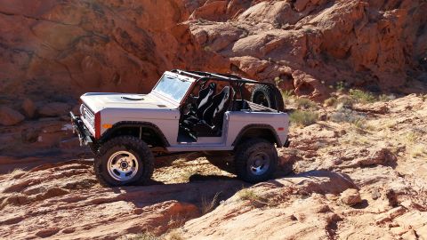 1979 Ford Bronco - A light gray, two-door Ford Bronco is parked on a rocky, desert terrain with large red rock formations in the background. The vehicle has i…