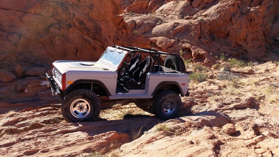 Light gray 1979 Ford Bronco with doors removed, parked on a rocky desert trail.