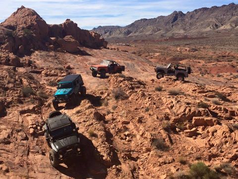 1979 Ford Bronco - Four off-road vehicles are navigating a rocky, arid landscape with mountains in the background. A dark gray Jeep is in the foreground, foll…
