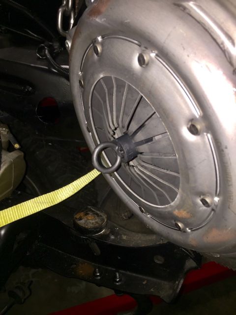 1978 Ford Bronco - A close-up view shows a vehicle's clutch assembly, with a yellow strap looped through a ring on the pressure plate and attached to a chain…