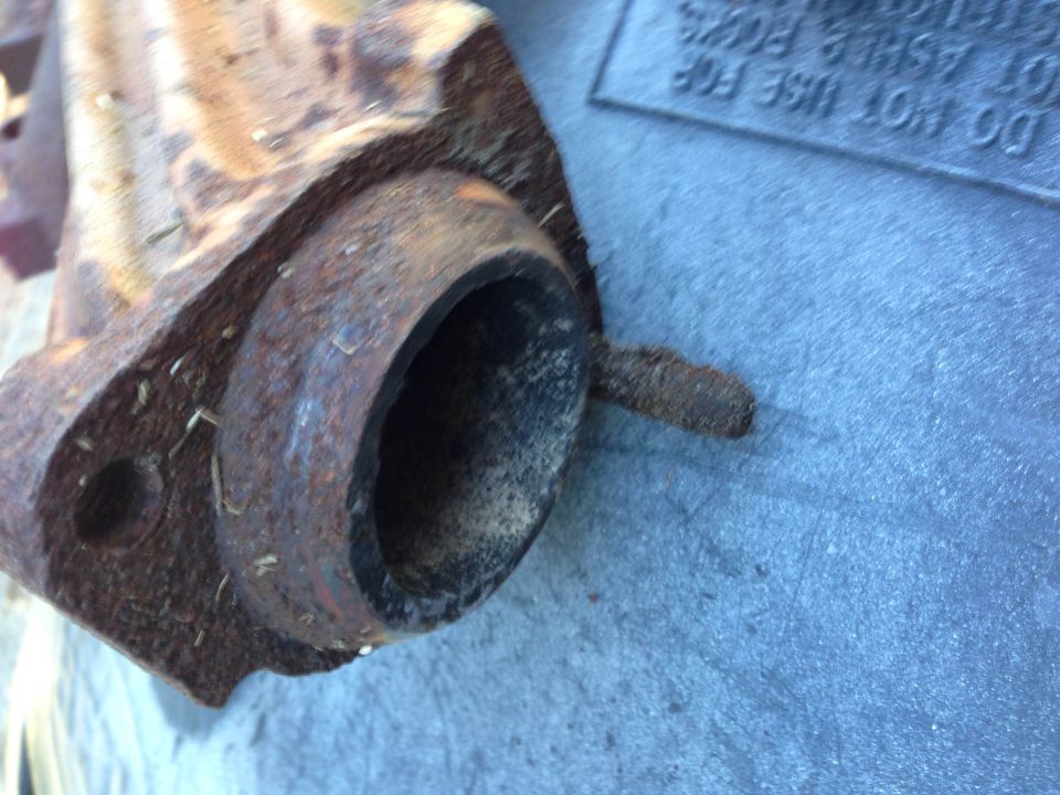 Close-up of a rusty exhaust manifold part with a circular opening.