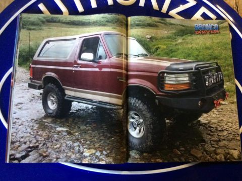1996 Ford Bronco - A maroon 1996 Ford Bronco is parked on a rocky stream bed with a brush guard and auxiliary lights on the front.
