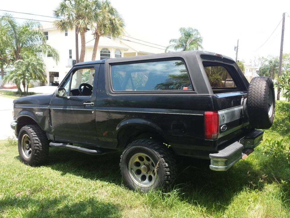 Black Ford Bronco parked on grass, rear passenger side view, spare tire on back