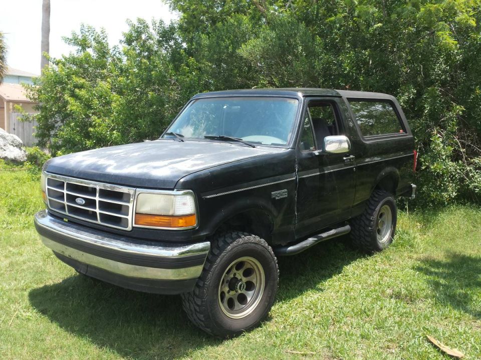 Black 1990s Ford Bronco parked on grass with trees in the background.