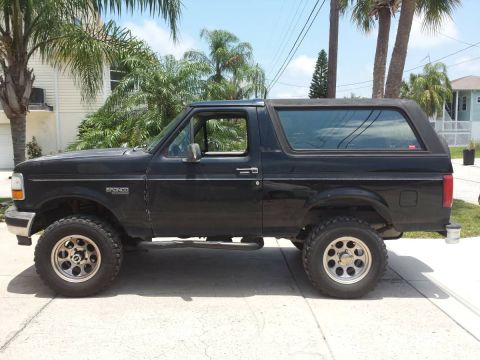 1995 Ford Bronco - The side profile of a black 1995 Ford Bronco is shown parked on a paved surface. The vehicle has aftermarket wheels and appears to be in a…
