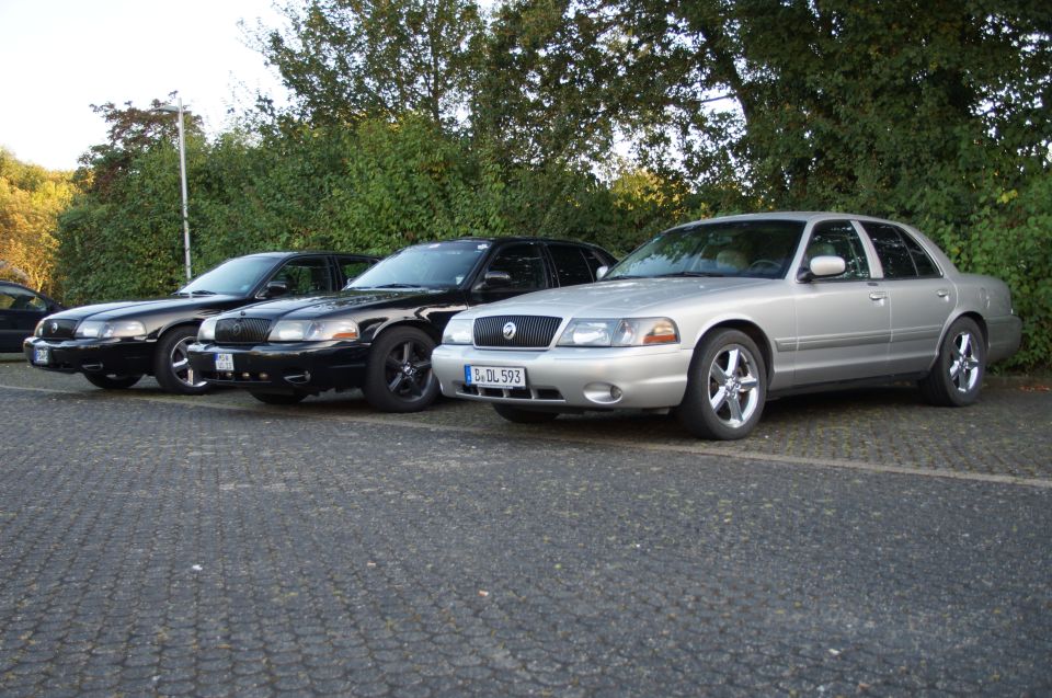 Three sedans parked in a row, a silver one in front and two black ones behind.