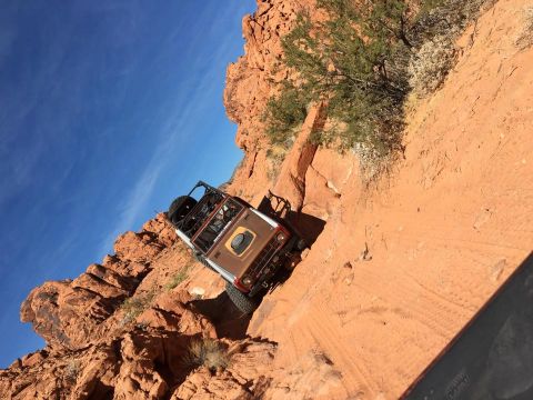 1979 Ford Bronco - An off-road vehicle navigates a challenging, narrow trail on a steep, red rock formation.