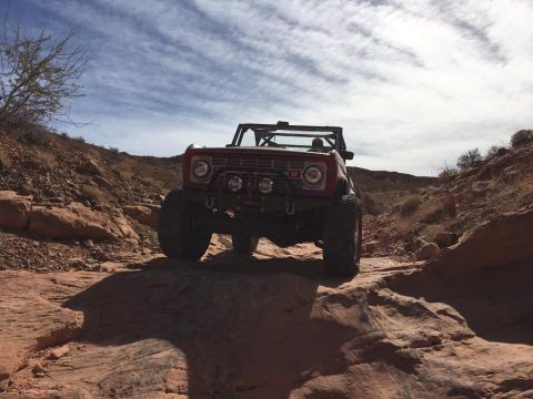 1979 Ford Bronco - A red 1978 Ford Bronco navigates a challenging rocky terrain under a cloudy sky.