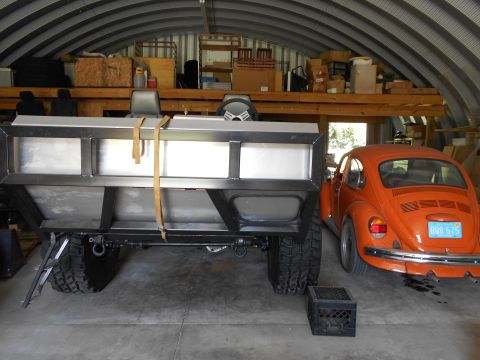 1992 Ford Bronco - An orange Volkswagen Beetle is parked in a garage next to a large custom trailer.