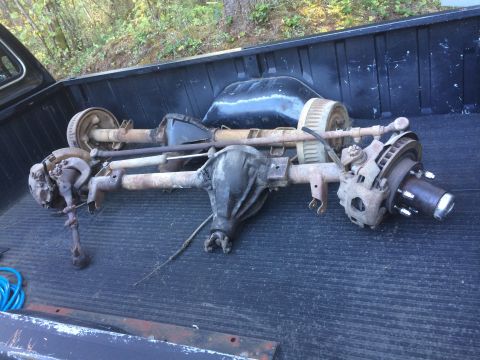 1962 Chevrolet Suburban - Vehicle axles and suspension components are loaded in the bed of a truck, with a blue hose visible.
