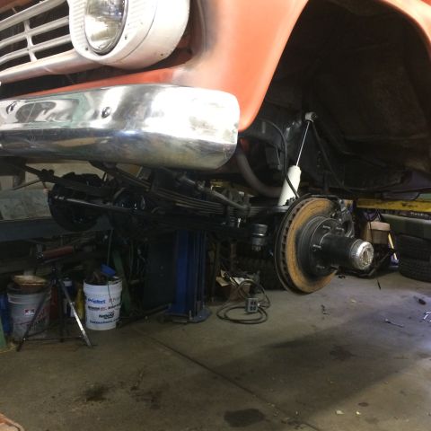 1962 Chevrolet Suburban - Front suspension and wheel assembly of an orange vehicle, likely from the early 1960s, undergoing work.