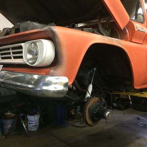 1962 Chevrolet Suburban - Front end of an orange pickup truck undergoing suspension work, hood is open.