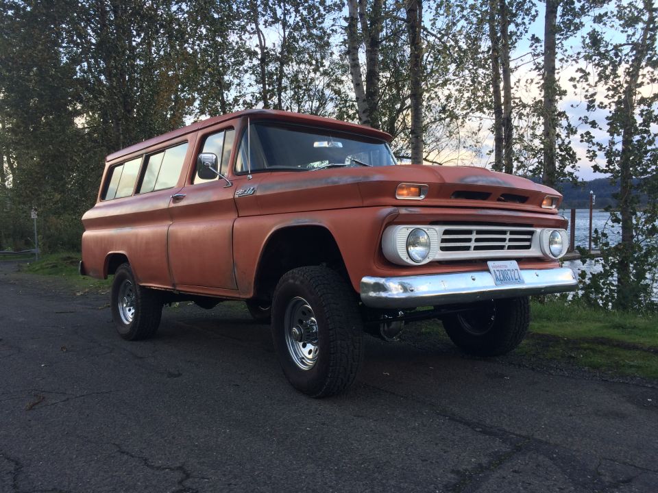 Orange Chevrolet Suburban with a lifted suspension and off-road tires, viewed from the front three-quarter angle