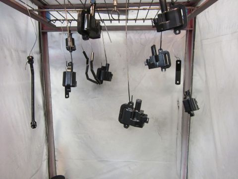 Black ignition coils and parts hanging to dry in a spray booth