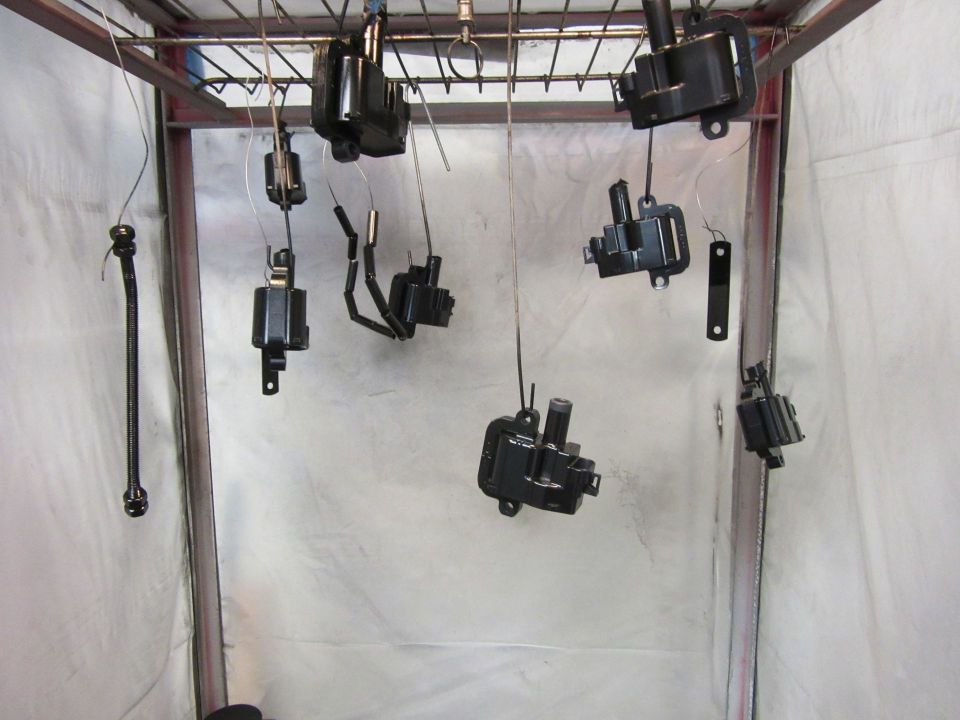 Black ignition coils and parts hanging to dry in a spray booth