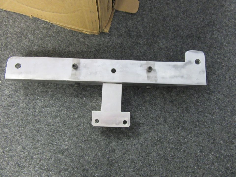 Aluminum bracket with multiple holes and a T-shaped mount, resting on gray carpet