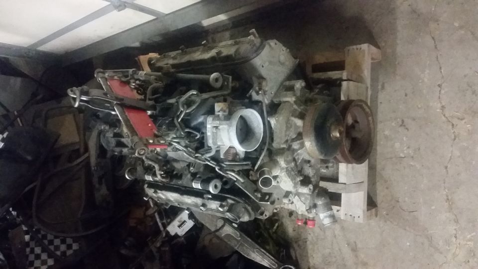 Engine assembly on wooden pallets, with red accents and various hoses and components visible