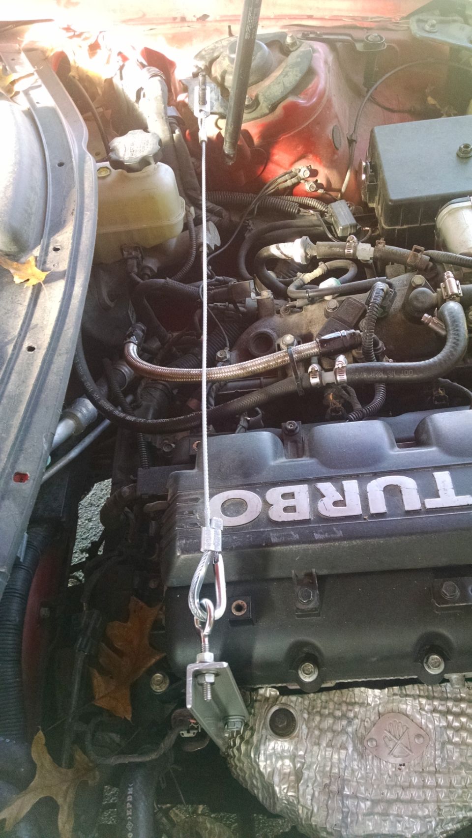 Engine bay with a cable attached to a clamp, obscuring part of the engine cover that reads "TURBO"