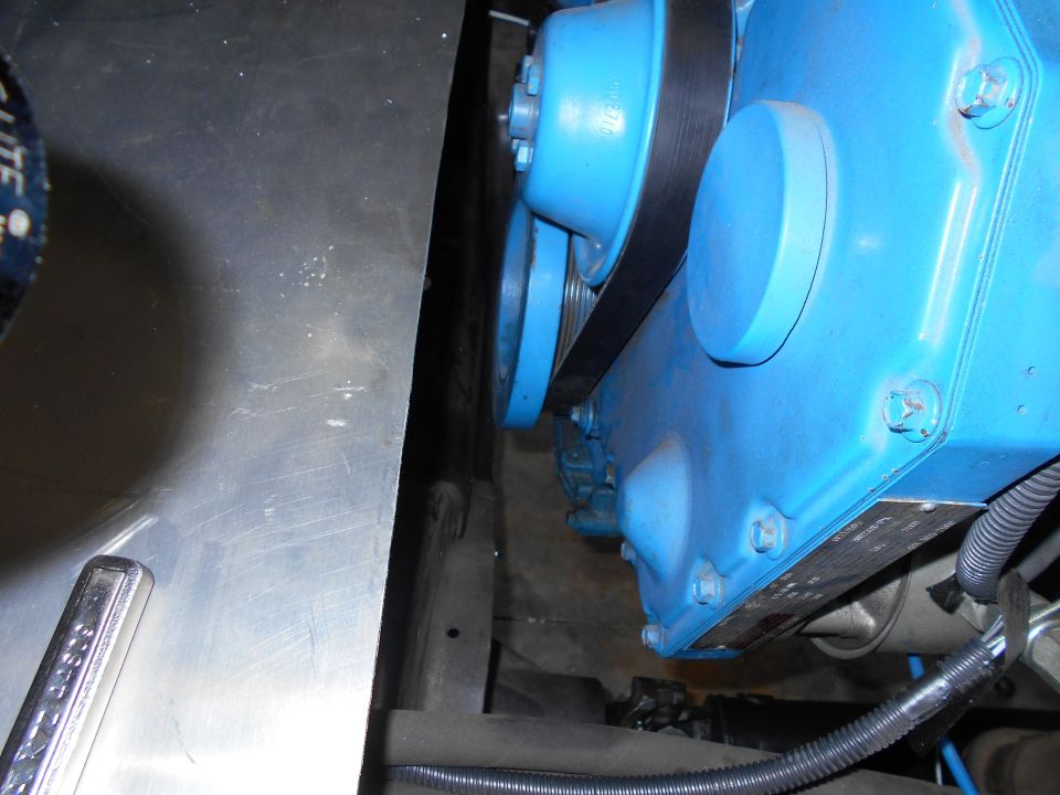 Blue engine component with a black belt and pulleys, next to a metal panel