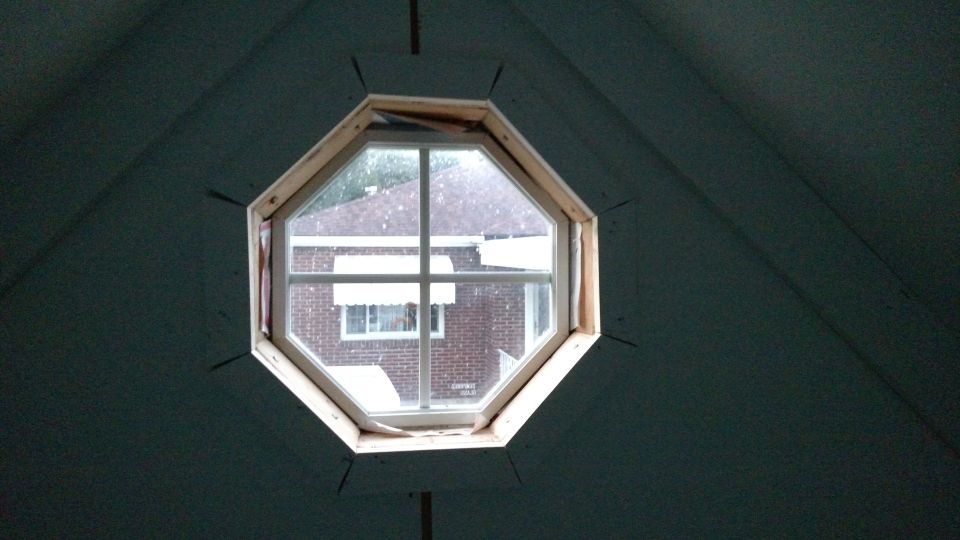 Octagonal window frame looking out at a brick house with white awnings