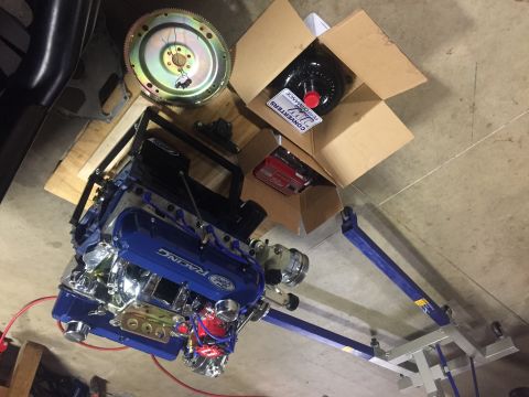 1982 Ford Bronco - A blue Ford Racing engine is displayed on a stand, accompanied by engine parts and boxes.