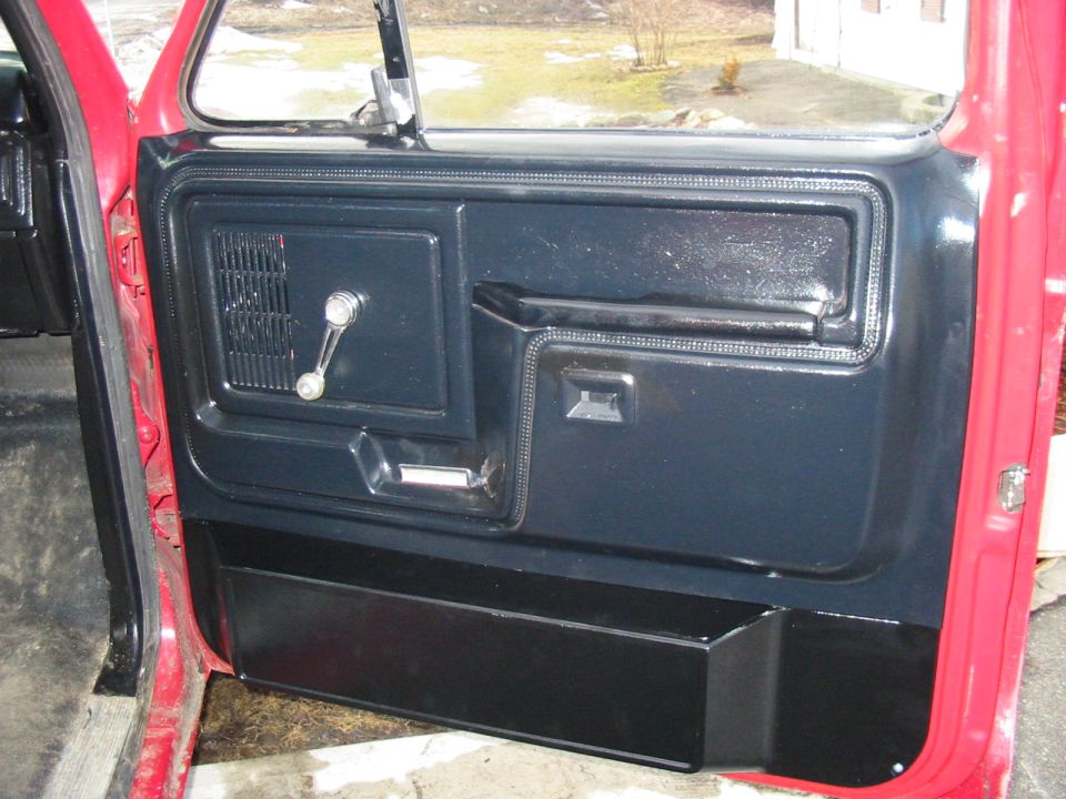 Red vehicle door panel with black interior trim, manual window crank, and armrest