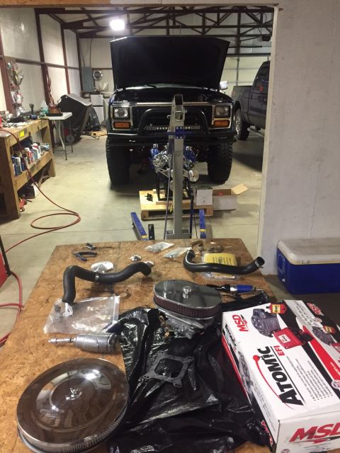 1982 Ford Bronco - A black 1982 Ford Bronco sits in a garage with its hood open and engine removed, while various parts are laid out on a workbench.
