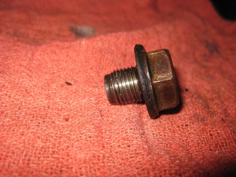 1994 Ford Bronco - An oil drain plug with a gasket is shown on a red cloth. Text at the bottom reads 'SUPERMOTORS'.