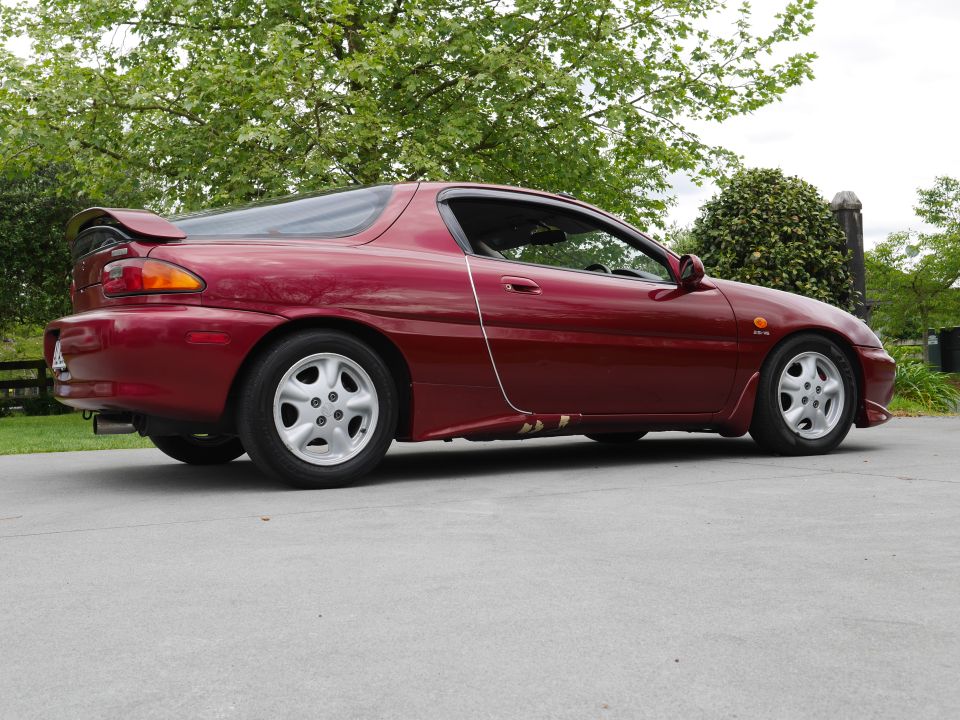 Red 1993 Mazda MX-3 coupe parked on concrete, side view