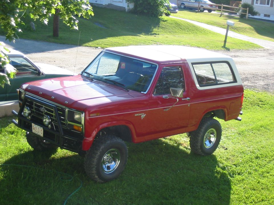 Red Ford Bronco with a white top parked on grass. It has a brush guard and off-road tires
