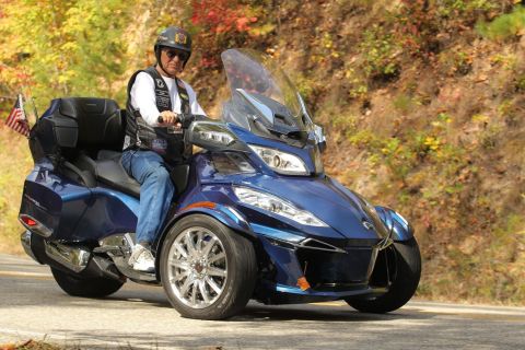 2014 Harley-Davidson FXDWGI Wide Glide - A rider cruises on a blue Can-Am Spyder F3-S on a scenic road with fall foliage.