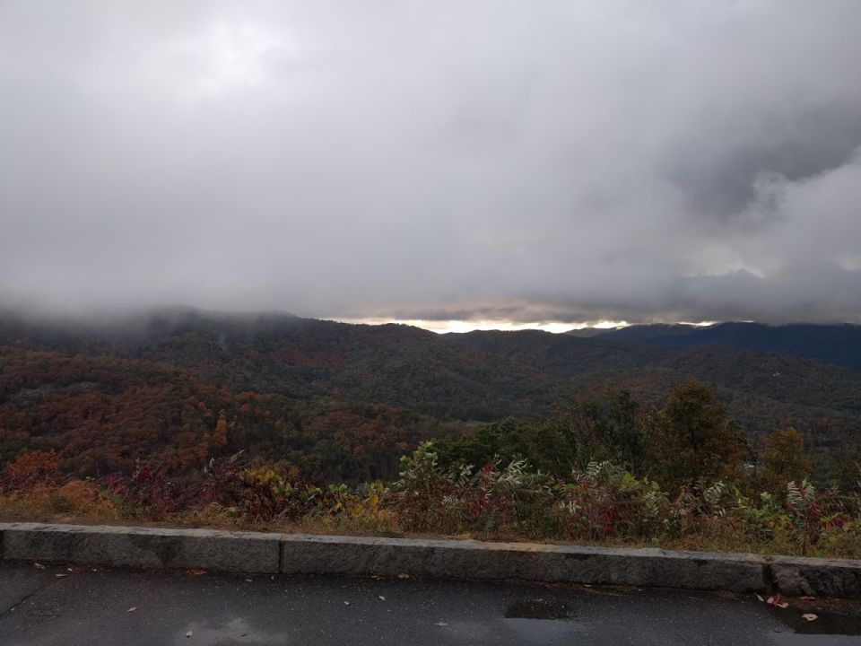 Mountain range under cloudy sky with autumn foliage and a roadside curb
